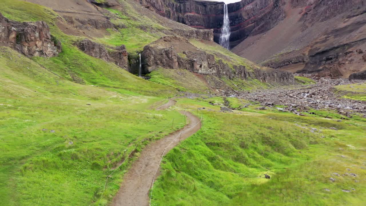 mujer caminando hacia una cascada con un impermeable amarillo