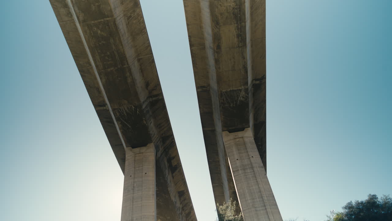 Low angle symmetrical view of concrete bridge pillars and parallel lines against a clear blue sky. Minimal architectural composition with strong perspective and geometric structure