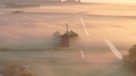 aerial view of traditional old windmill in a meadow with low fog at sunrise, friesland, netherlands