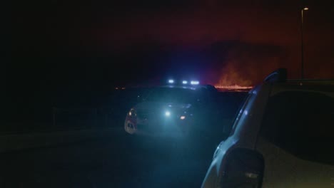 a police car blocks a road as fire and lava from the grindavik volcano in sundhnúkur crater, iceland, erupt in the distance.