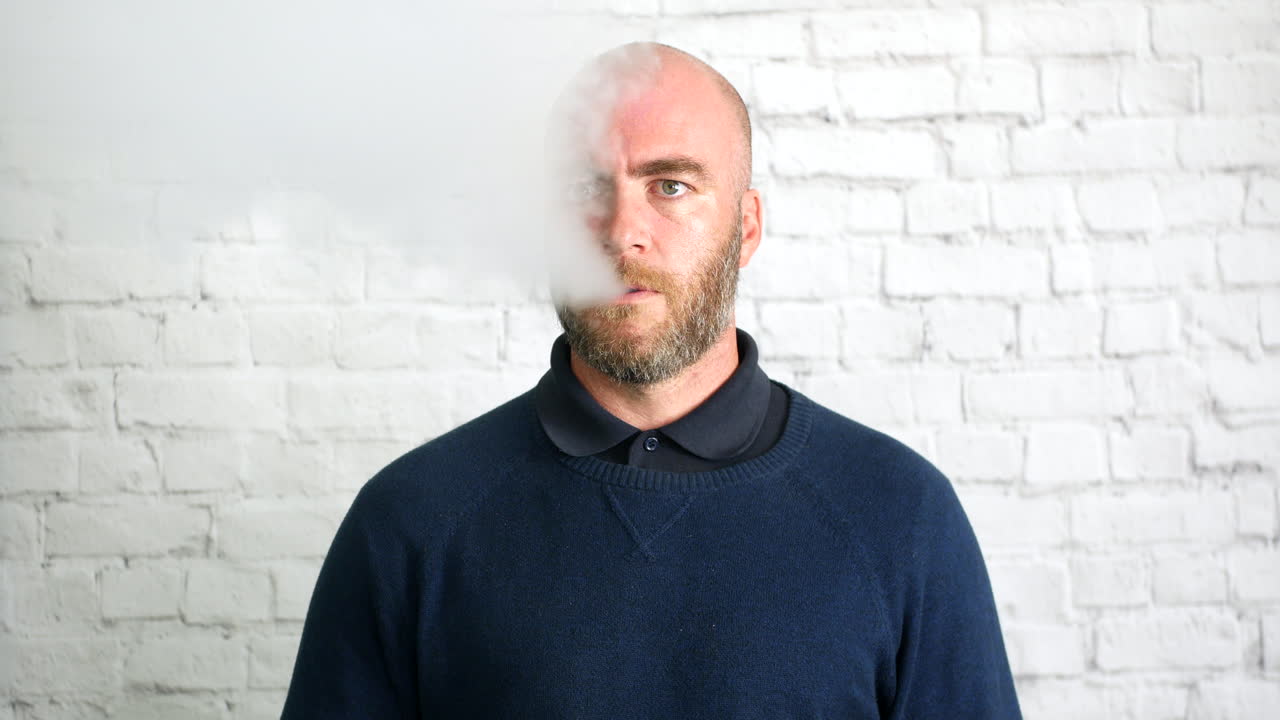 연기 구름과 함께 흰 벽 앞에서 실내에서 베이핑하는 남자의 초상화