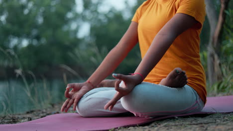 tight shot of a woman sitting in padmasana pose on yoga mat at outdoor