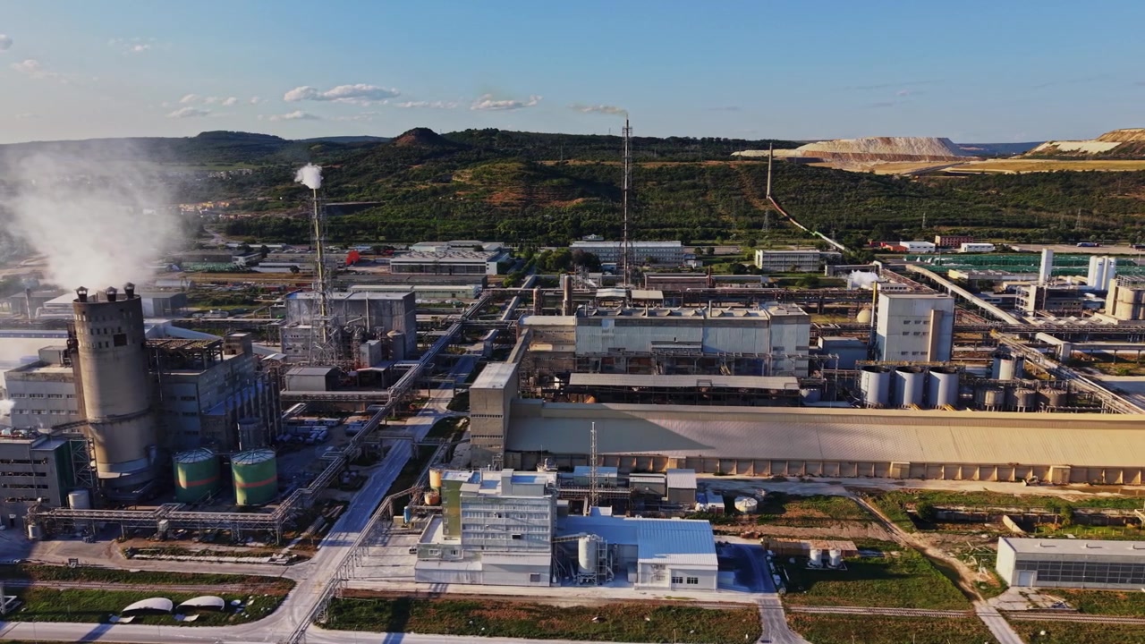 Factory site with smokestacks and green hills in the background