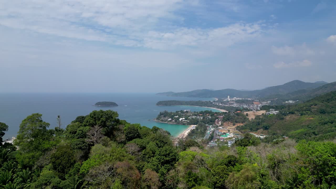 Aerial view of tropical Kata Noi Beach in Phuket, Thailand, with turquoise water, lush hills, and coastal town.