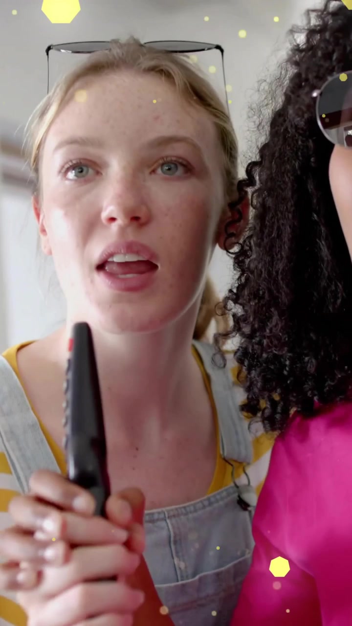 Animation of yellow lights over two diverse teenage girls miming singing with tv remote control