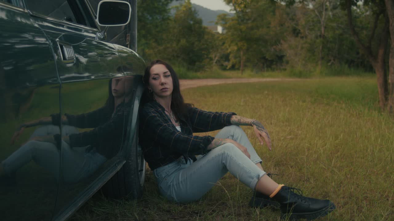 Woman Sitting Beside a Vintage Car in a Park