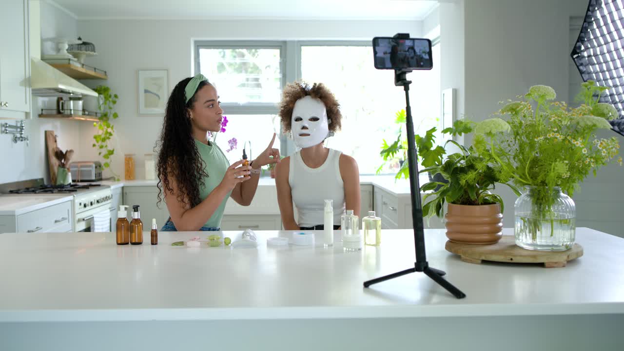 Donne afroamericane che salutano la telecamera, treppiede per telefono che inquadra la conduttrice che dimostra un siero con contagocce