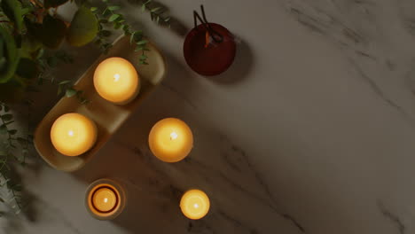 overhead view looking down on still life of lit candles and incense stick with green plant as part of relaxing spa day decor 1