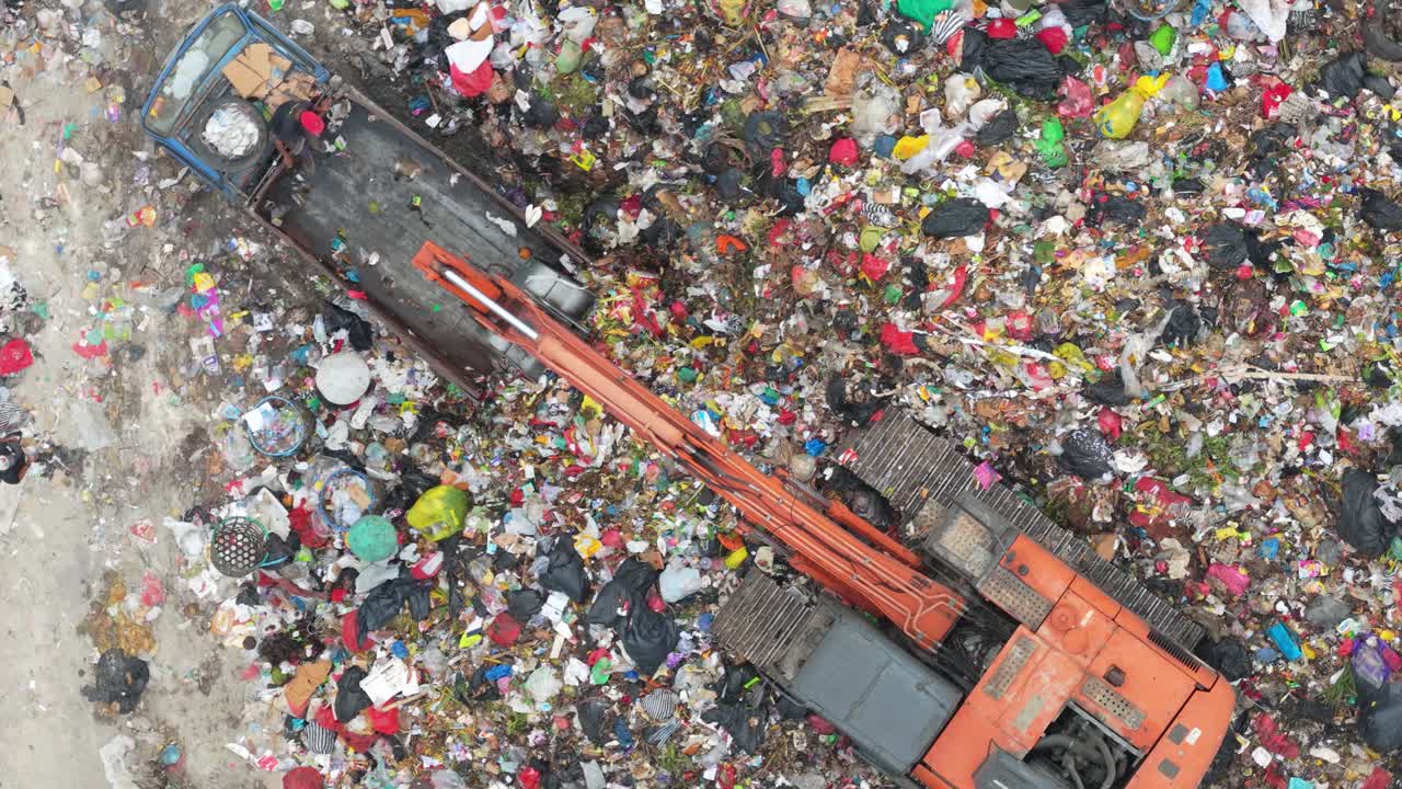 Vista aerea di un escavatore che movimenta rifiuti in una grande discarica.