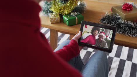 Hombre-Caucásico-Saludando-Y-Usando-Una-Tableta-Para-Una-Videollamada-Navideña-Con-Una-Familia-Sonriente-En-La-Pantalla