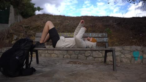 young caucasian man resting on park bench after exhausting hiking day