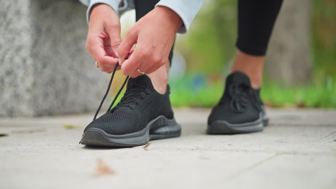 Close-up of sport fair lady tightening one of her black sneaker shoelaces, wearing rings on both hands, preparing for workout, focused on footwear and active lifestyle, ready for exercise