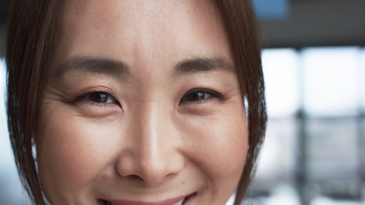 미묘한 메이크업과 어두운 머리카락을 가진 미소 짓는 아시아 사업가의 클로즈업