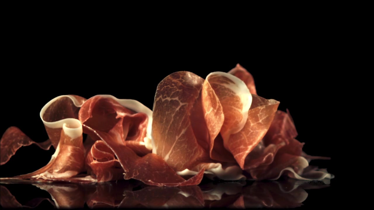 Tranches de prosciutto tombant au ralenti sur fond noir.