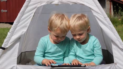 two toddlers looking at tablet in tent outdoors, twins