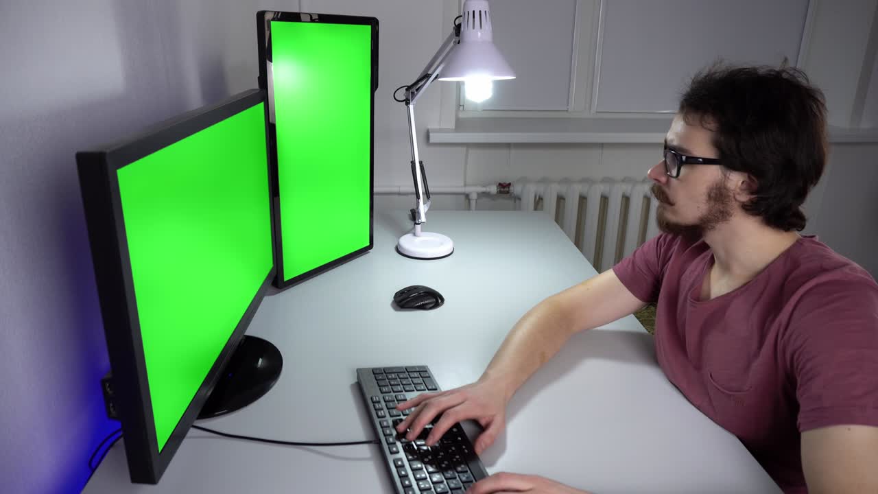 un joven en la oficina está trabajando en una computadora con dos monitores con pantalla verde
