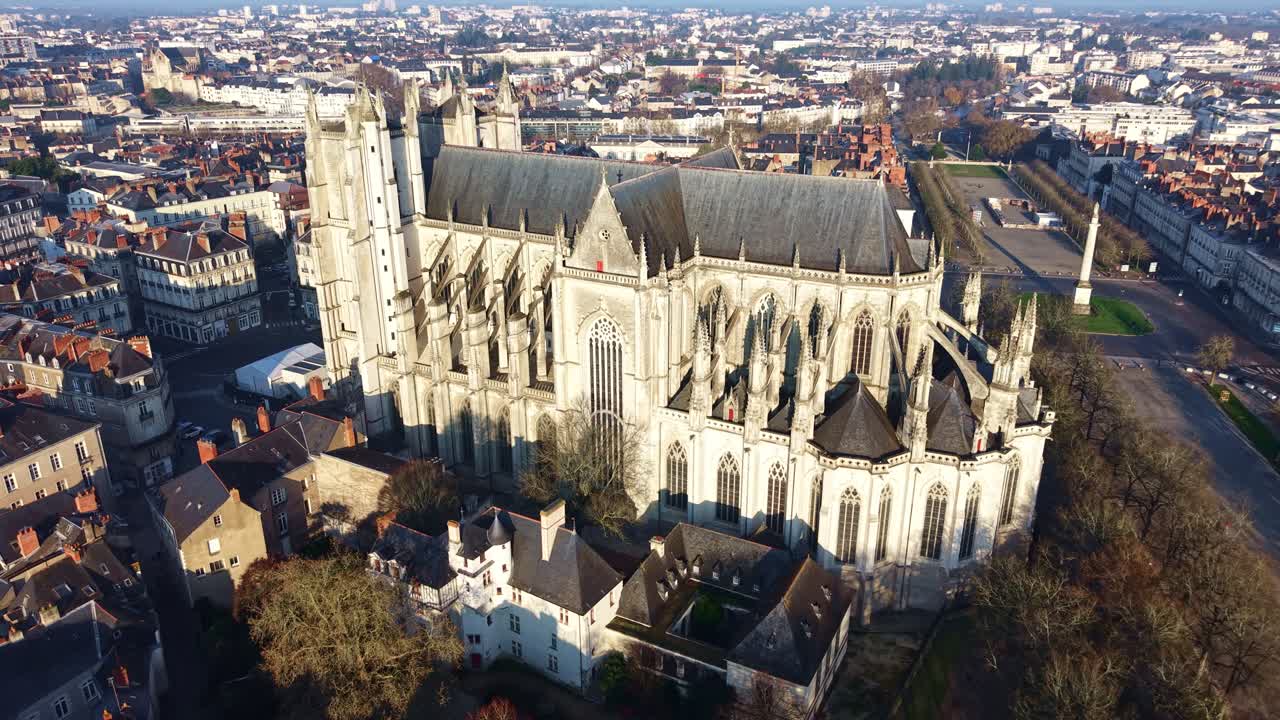 Vista aerea orbitante della Cattedrale dei Santi Pietro e Paolo di Nantes, in Francia, con la sua architettura gotica in pietra che domina il paesaggio urbano storico, mentre Place Maréchal Foch e la Colonna Luigi XVI