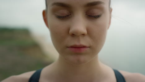 girl take deep inhale with closed eyes meditating yoga on seashore close up.