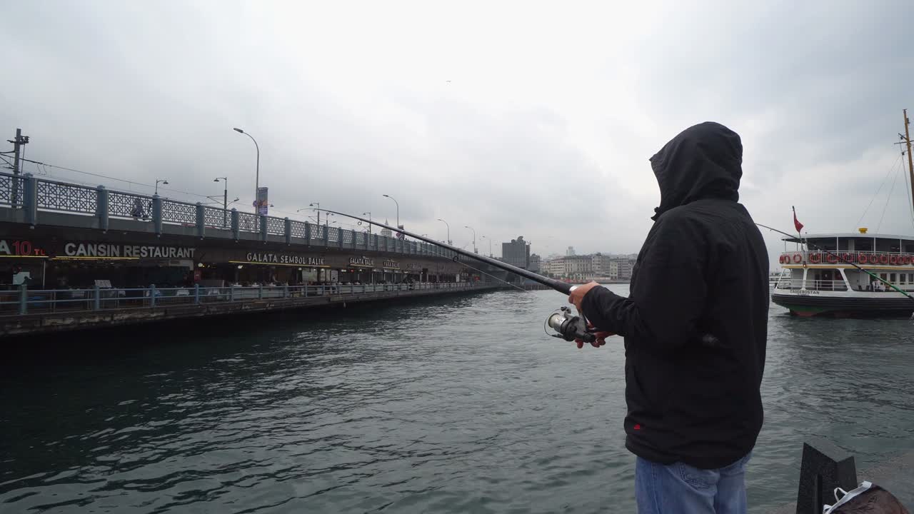 человек ловит рыбу на мосту галата в дождливую погоду