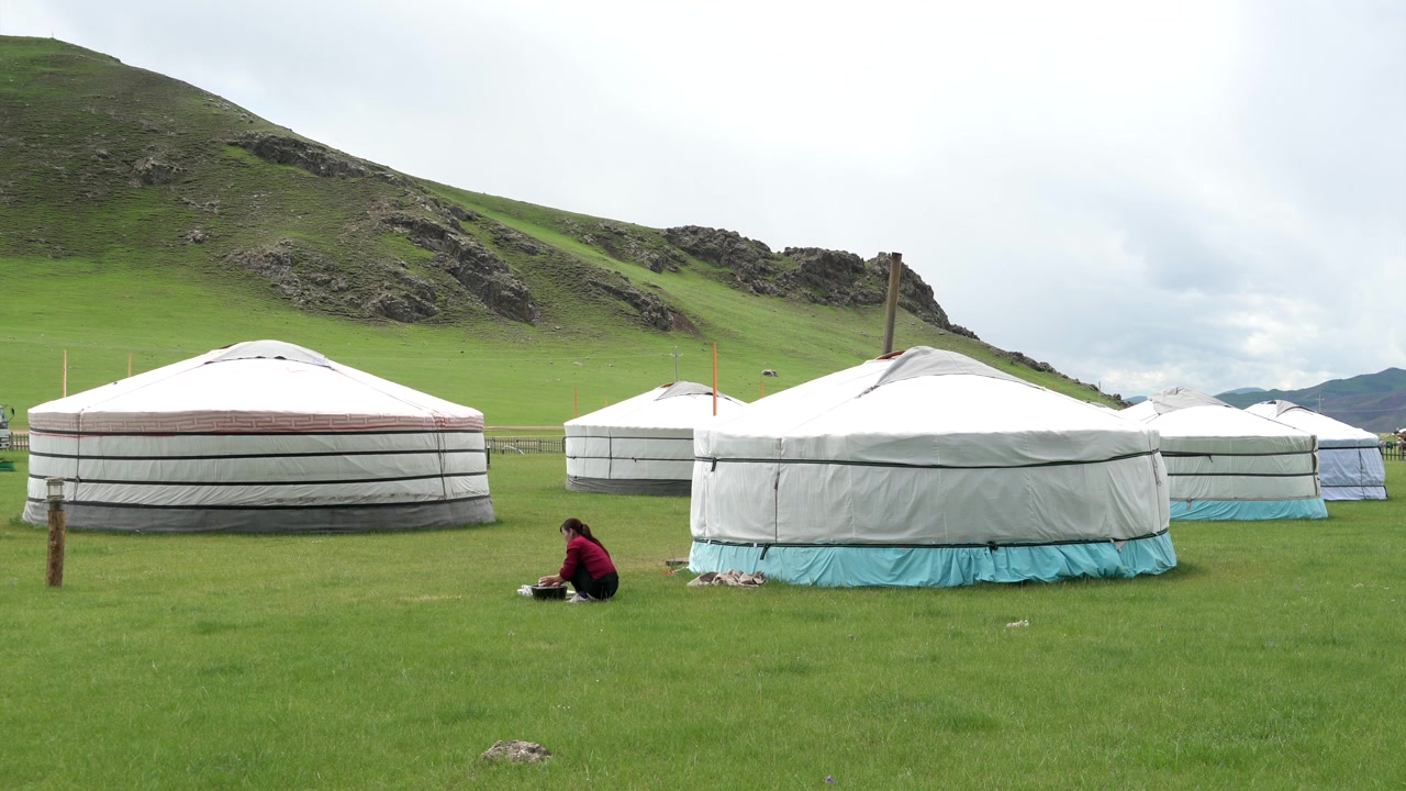 Kvinna sitter på gräs nära traditionella mongoliska jurtor