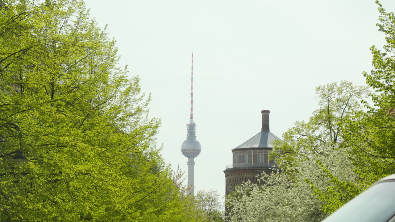 la torre de televisión de berlín se alza en la distancia, el cielo azul en el fondo, los árboles verdes en primer plano