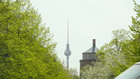 he-Berlin-Television-Tower-stands-tall-in-the-distance,-Blue-Sky-in-the-background,-green-trees-in-the-foreground