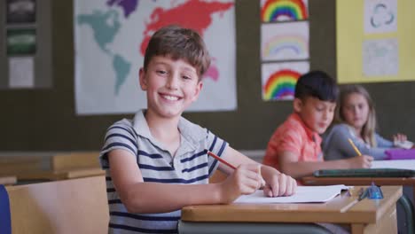 Junge-Lächelt,-Während-Er-In-Der-Schule-Auf-Seinem-Schreibtisch-Sitzt