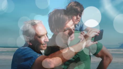 Animation-of-bokeh-over-happy-caucasian-grandfather,-father-and-son-taking-selfie-on-beach