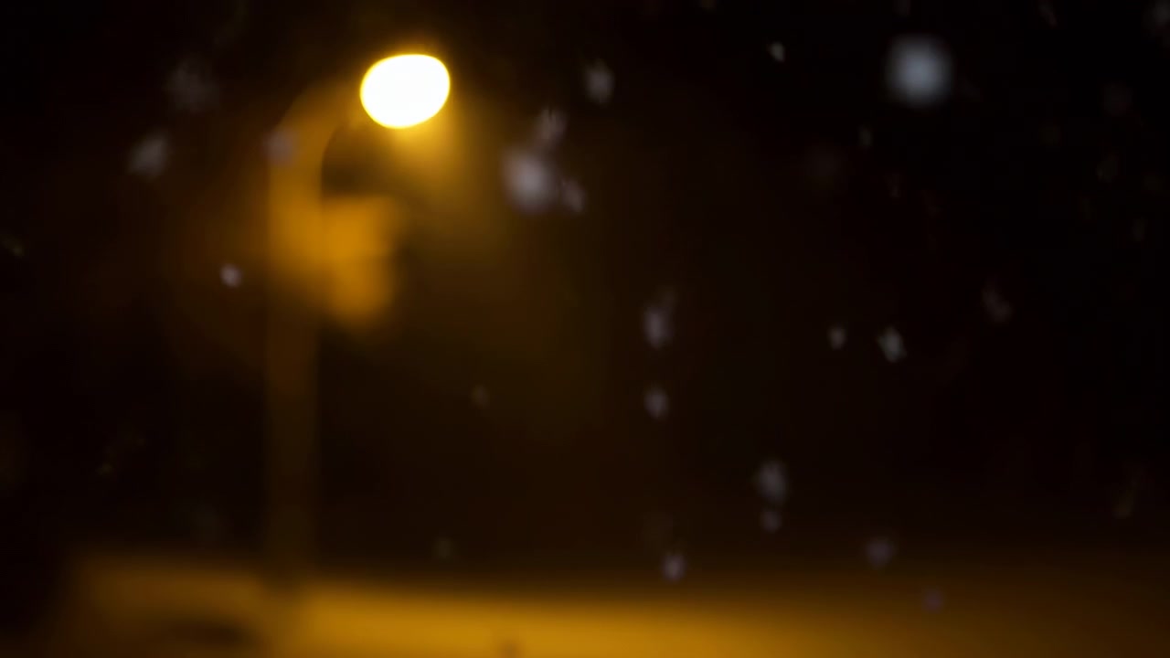 Snow Falling Under Amber Streetlamp, Soft Bokeh Flakes Drifting Through Halo Glow, Empty Urban Pavement