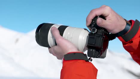 detail of caucasian male hands holding up a camera and photographing winter snowy mountain landscape