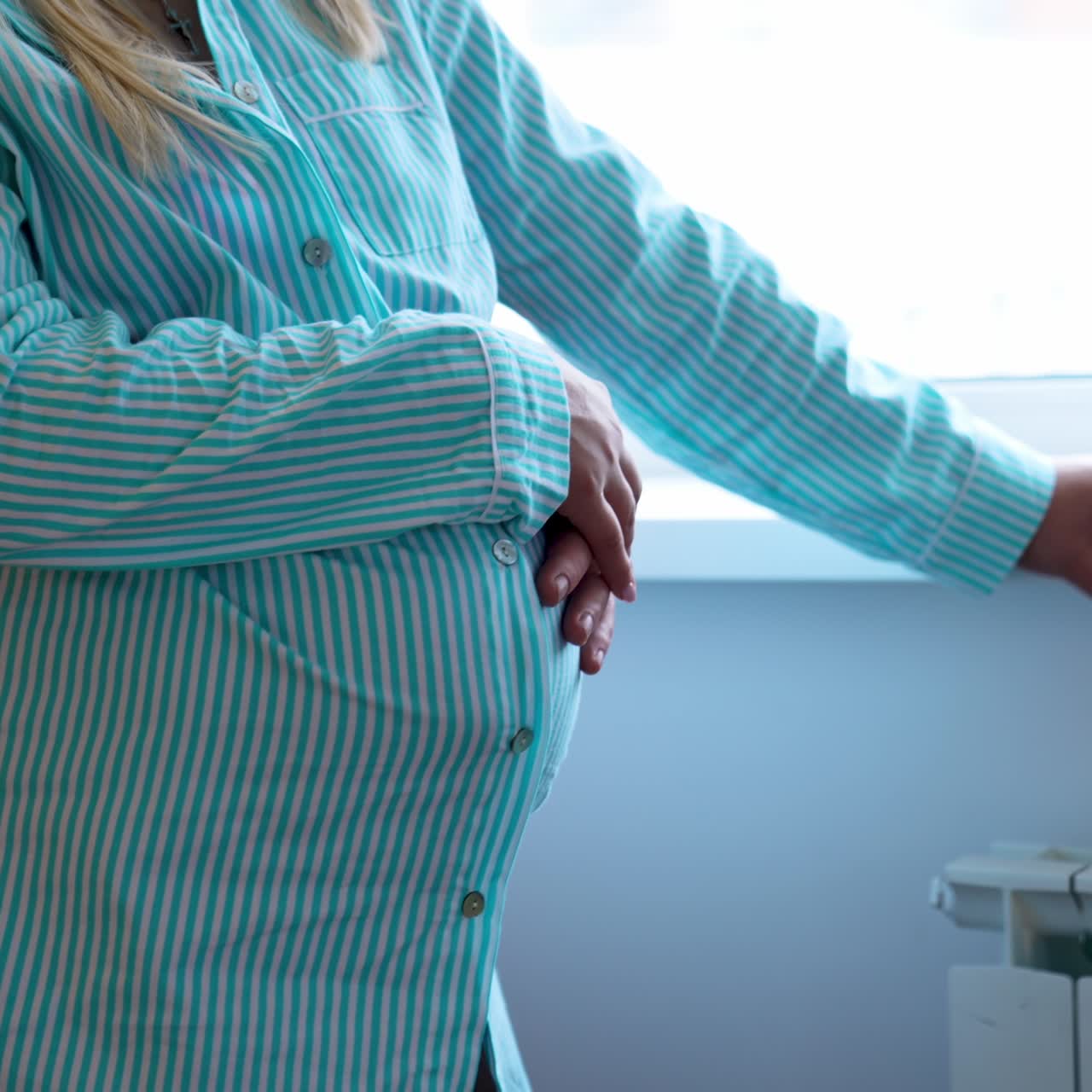 Man embracing his pregnant wife from behind. Couple swaying slowly standing near the window-sill