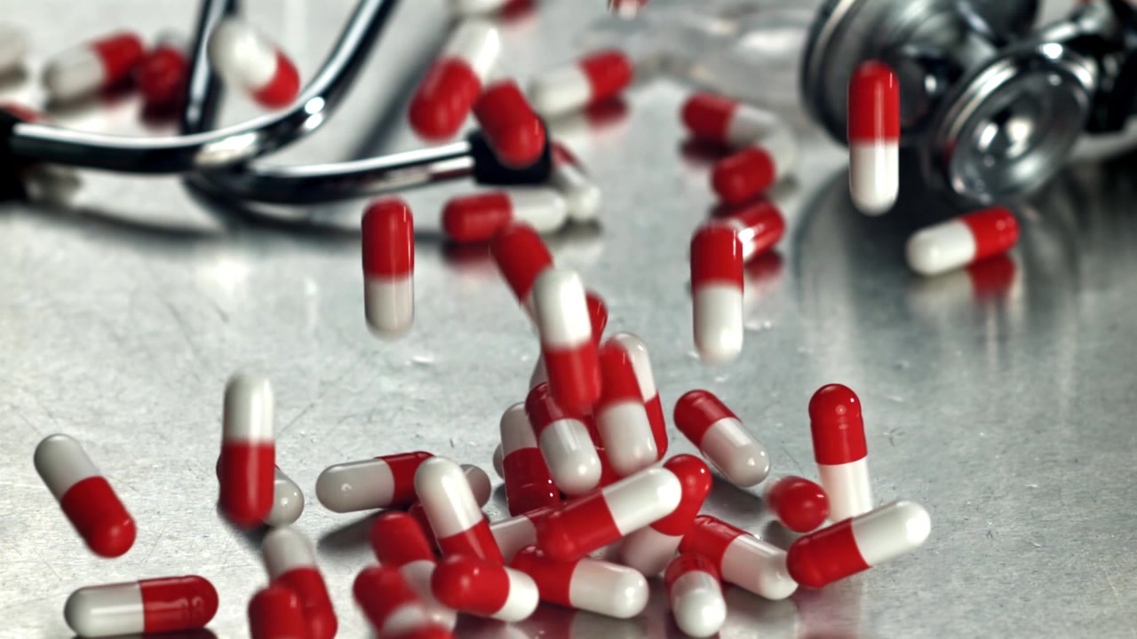 Capsule mediche rosse e bianche che cadono su una superficie metallica