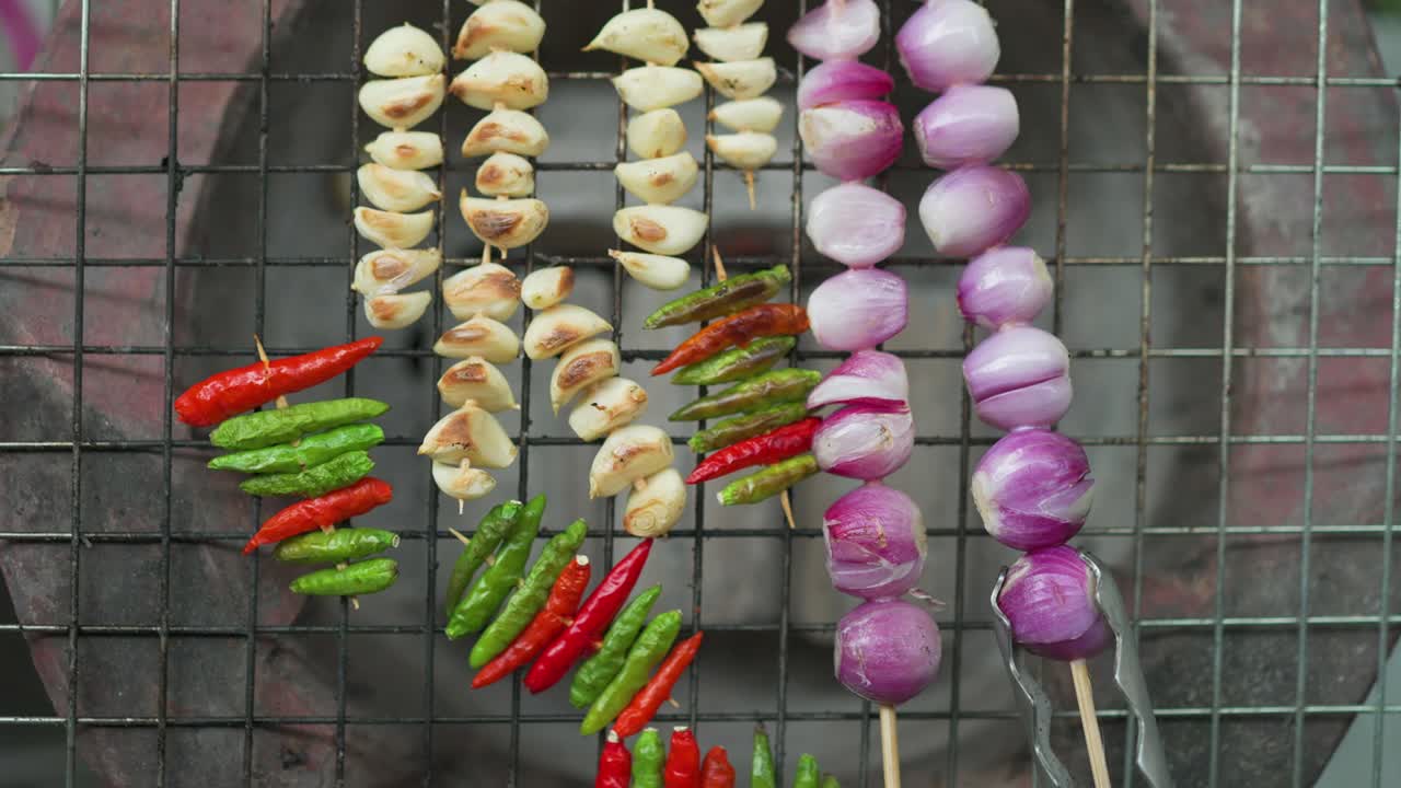 Top view of grilling garlic chilies and onion on grates and charcoal.