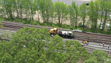 an aerial view over trees looking at men fixing train tracks on a sunny day