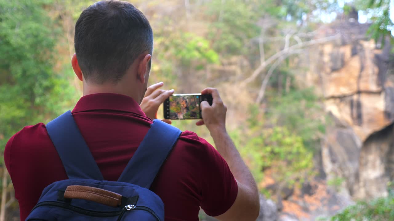 fotógrafo de senderismo de montaña o videoblogger hombre filmando un cañón en un teléfono celular. viajero con una mochila videógrafo. capturando paisajes y naturaleza con una cámara panorámica de teléfono inteligente. vista trasera.