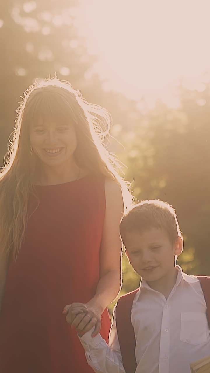 lady with long loose flowing blond hair walks with children in school uniform against trees at back sunlight slow motion
