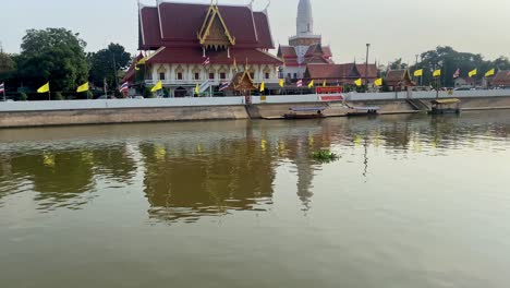 golden sunlight reflects on the river by a thai temple with traditional architecture, boats docked