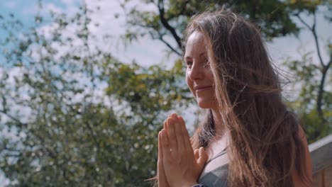 a beautiful young woman looking straight with hands together on the chest meditating in nature - medium closeup shot