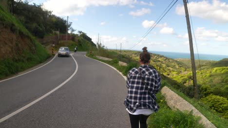 woman walking on scenic mountain road with ocean view