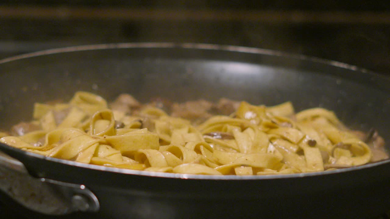 Hand Removing Stainless Steel Lid to Reveal Italian Mushroom Tagliatelle Simmering in Hot Pan with Various Fungi Including Champignon, Shitake, Nameko. Home Cooked Cream Sauce Based Pasta Dish.