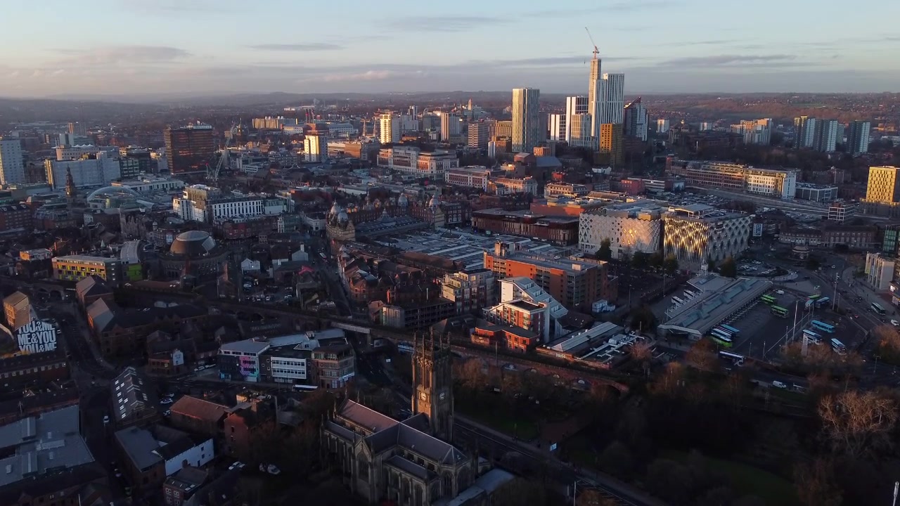 Volo aereo sulla città di Leeds verso edifici moderni al tramonto, Regno Unito