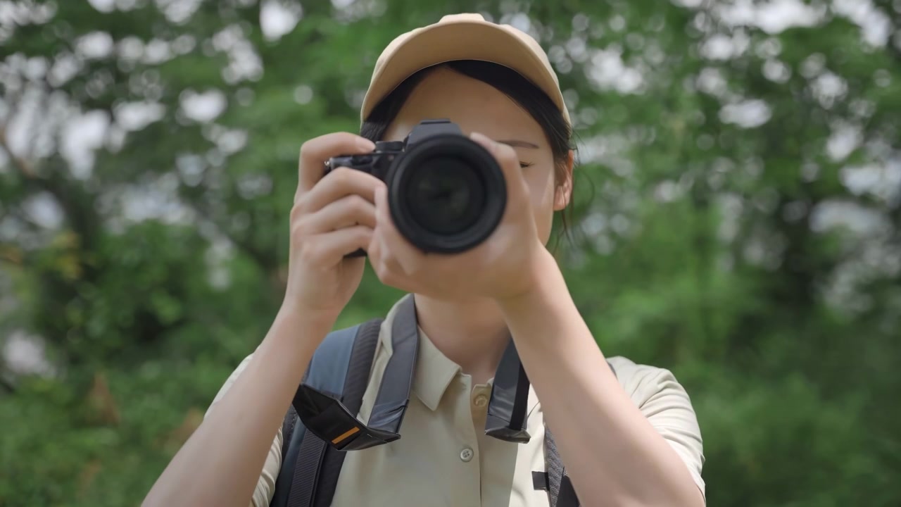 大きなバックパックを背負いトレッキングウェアを着た女性写真家が、デジタル一眼レフカメラを顔に構え、美しい自然の森の風景を撮影している。旅行、冒険、アウトドア探検。