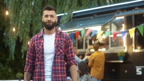 Portrait-Shot-Of-Handsome-Young-Man-Standing-In-Front-Of-Camera-And-Smiling-Cheerfully-Outdoors