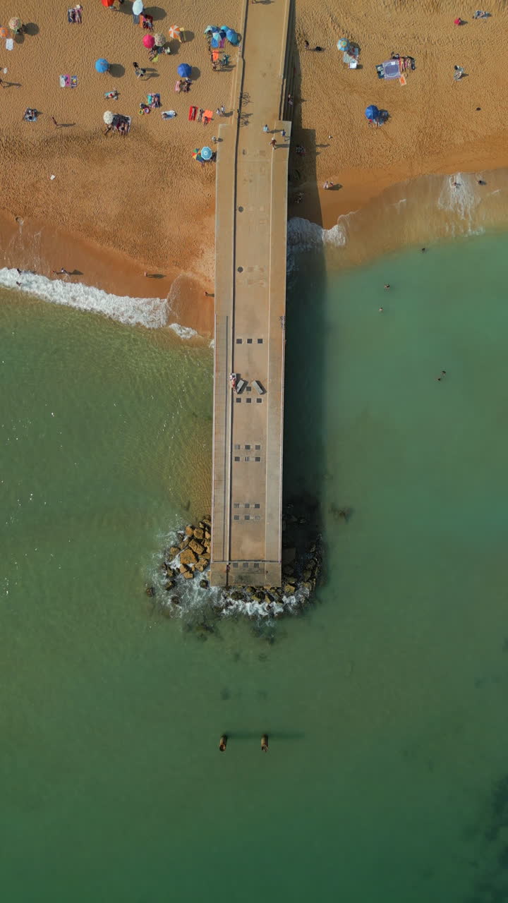 Vertical video, descending drone view over pontoon with turquoise clear water, Albufeira