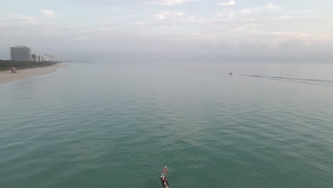 Paddleboarder-and-boater-are-only-people-on-misty-morning-beach,-Miami