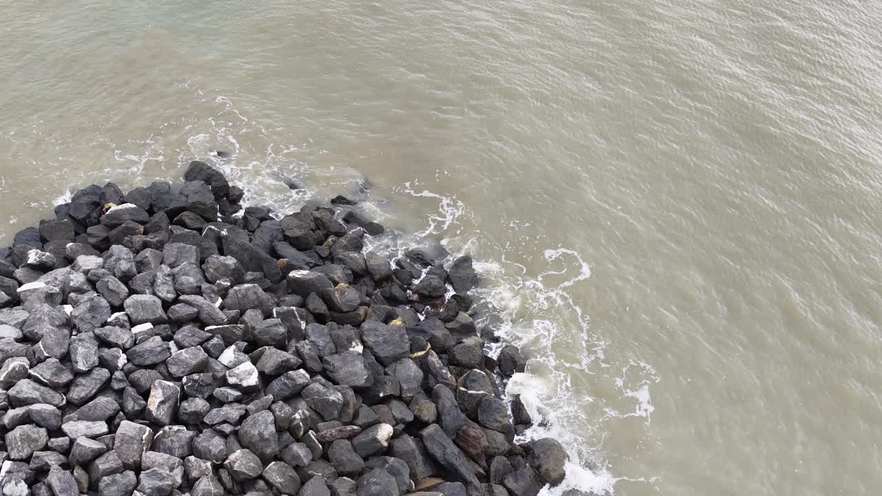 Top-down view of a rocky breakwater meeting ocean waves, showcasing natural coastal protection