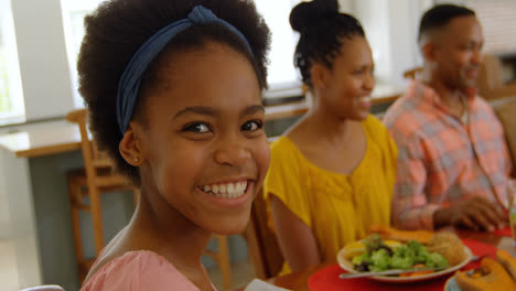 Vista-Frontal-De-Una-Niña-Negra-Comiendo-Con-Su-Familia-En-La-Mesa-Del-Comedor-En-Una-Casa-Cómoda-4k