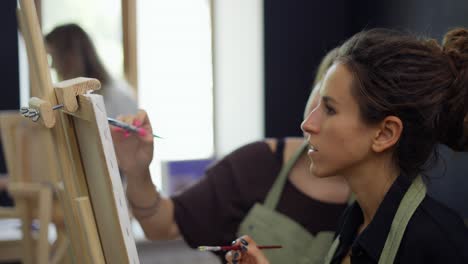 student and art teacher during painting lesson standing in front the easel, close up