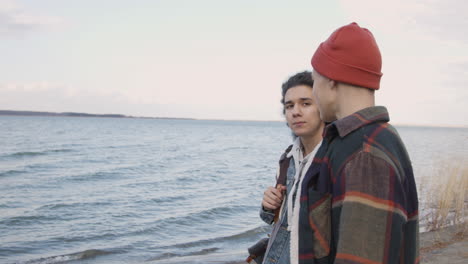 Side-View-Of-A-Teenage-Boys-Talking-Standing-Near-Of-Seashore-On-A-Cloudy-Day