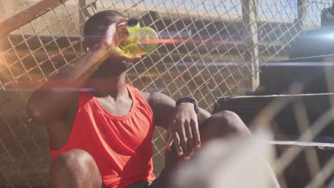 Animation-of-glowing-lights-over-an-exercising-african-american-man-drinking-water